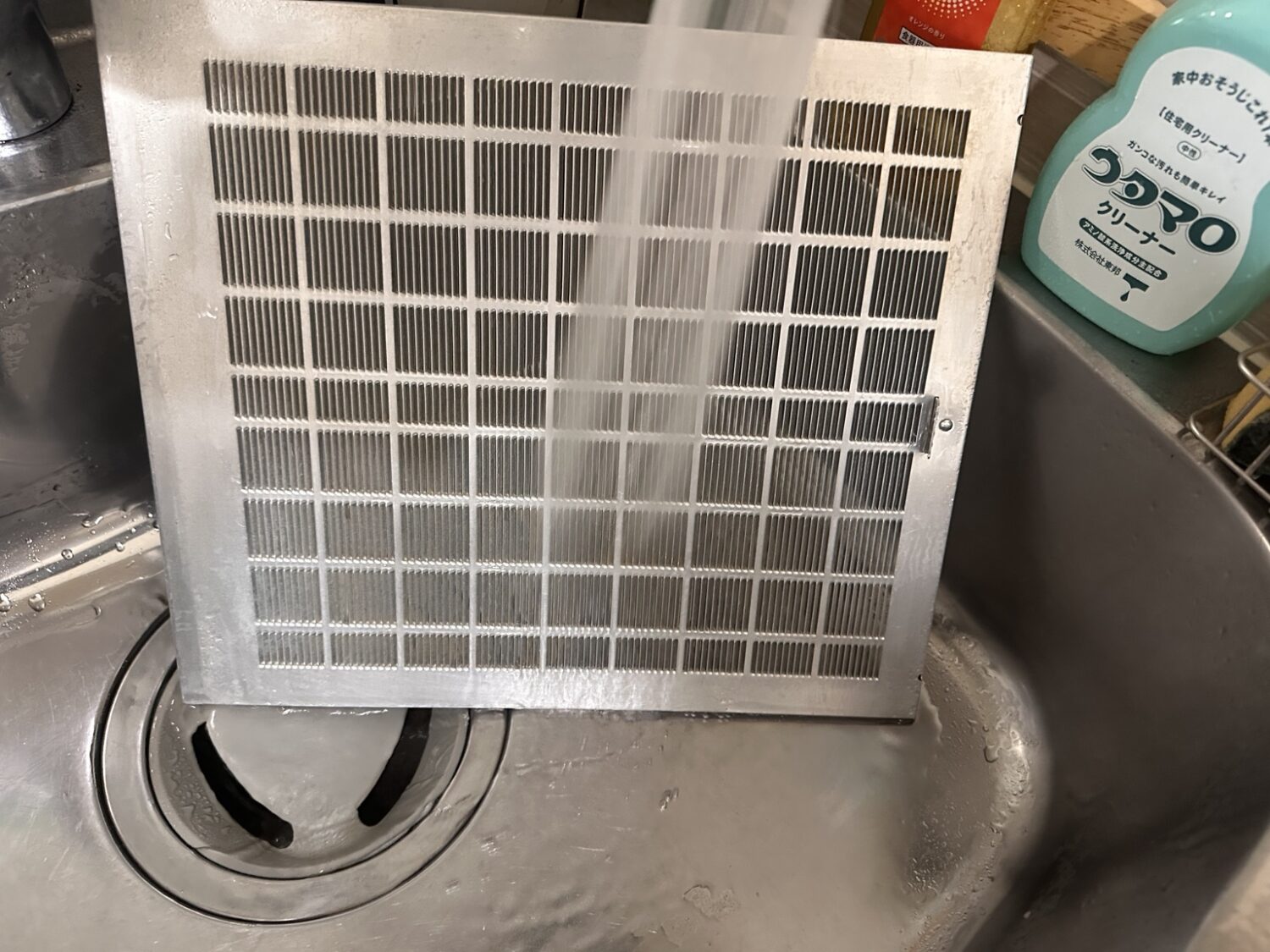 レンジフードフィルターをすすいだあと水気を拭き取って仕上げている様子